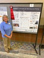 Woman - Joetta White - standing on left next to poster titled TENNESSEE GRAIN BIN SAFETY & RESCUE AWARENESS TRAINING with red ribbon on it that is tit