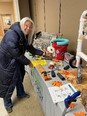 Woman with long white hair wearing calf-length dark coat in front of TN AgrAbility display table with fall decorations and assistive technology tools on it