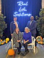 TN AgrAbility staff - 2 men standing & 2 women seated - against blue curtained backdrop with lighted sign reading REAL LIFE SOLUTIONS