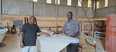2 Ugandan men standing in large workshop beside a white boat. Man on left is Mutumba Faisal.