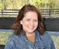 Portrait from chest up of Eileen Legault smiling at camera with farm fence in background.