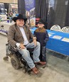 Man in wheelchair wearing black Stetson had with little boy standing next to him with same kind of hat.