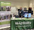 Kendra Martin standing behind AgrAbility for Pennsylvanians display table with AgrAbility banner on left