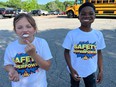 A white girl and a black boy smiling with food in their mouths and wearing t-shirts saying SAFETY IS MY SUPERPOWER