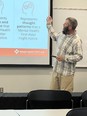 Man with a beard teaching and gesturing toward a slide screen showing a Mental Health First Aid picture