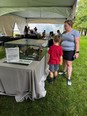 Woman with a little boy in front of her looking at tabletop display under a tent
