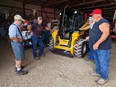 Four men looking at a skidsteer in a large shed on the Stinson farm