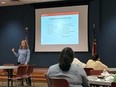 A woman using PowerPoint while teaching in front of a classroom