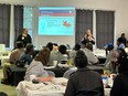 Two women speaking to a large racially diverse crowd in a classroom with a PowerPoint slide behind them