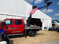 Red LifeLyfts flat-bed truck with lift extended against a backdrop of a large white tent