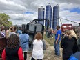 Farmer showing equipment to OT & PT students with 3 large blue  silos in the background