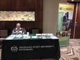 Jim Craig seated behind a CO State University Extension - AgrAbility display table at FALCON conference