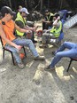 A group of loggers seated on chairs outside with a woods in the background