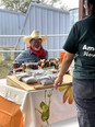 Man in cowboy hat red neckerchief & denim shirt with clown face makeup staffing a HarvestFest booth