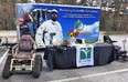 A trackchair on the left next to the GA AgrAbility display table on the right in a parking lot with the Farm Again trailer in the background.