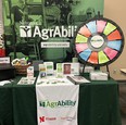 NE AgrAbility booth showing table with brochures - spinning wheel game - and NE AgrAbility banner in background.