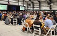 Large crowd of people eating around round tables in large event center.