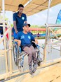 A young African man standing behind a wheelchair with a youth in it on a boat on Lake Victoria