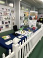 FL AgrAbility booth with AgrAbility materials and small AT behind picket fence in a room.