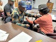 2 men and 2 women  all African American  doing activities at long tables in a room