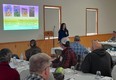 Abbie Spackman speaking to people in a room at long tables with PowerPoint presentation on wall next to her