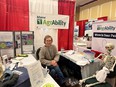 Toni Small sitting at ME AgrAbility table with various posters and props around her including a skeleton also seated at the table.