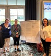 2 women standing on the left and 1 on the right of a research poster