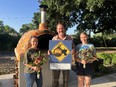 2 young women - one on each side of a man holding a sign advertising Pizza for Producers with a wood-fired oven behind them