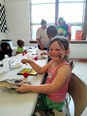 A young girl with face paint whiskers working at a long table at Clown College