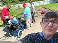 Selfie photo of a woman with people behind her who are working with a man in a wheelchair to help water some garden beds