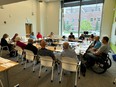 A group of people around long tables in a square in a conference room with a large window at the back.