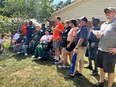 A group of people standing outside in a line watching something with 3 of them in wheelchairs.