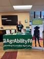 AgrAbility for Pennsylvanians booth in a large room with a stand-up banner with the silhouette of aperson on it reading HOW CAN ASSISTIVE TECHNOLOGY HELP ME