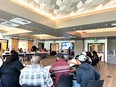 People at long tables in a large conference room listening to a speaker in front with PowerPoint