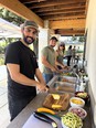 2 men and a woman working at a long table outdoors preparing food for Pizza For Producers