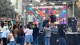 Live band on open stage in downtown area with banner behind them YOLO FARMWORKERS FESTIVAL  and people watching them