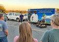Mason Dean outside next to Farm Again trailer and Trackchair talking to a group of people