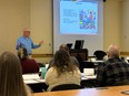 Joe Ricker teaching using PowerPoint with several people in front of him listening at long tables