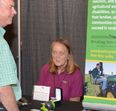 Linda Tarr at trade show booth talking with man next to AgrAbility display
