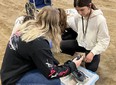 3 girls looking at assistive technology outside on the ground with a wheelchair in the background