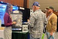 Young woman - Kara - on left talking with 2 men on rt in front of AgrAbility exhibit table