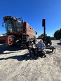 2 men sitting in front of a combine - 1 in a wheelchair and the other sitting on a folding chair