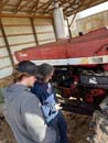 A man & woman in a farm shed looking at a large older International tractor