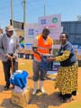 A Ugandan man presenting a woman with a gas burner as another man looks on