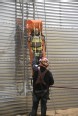 Person wearing personal protective equipment while lowering a practice dummy down the side of a grain bin 