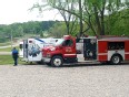 A fire truck with an ambulance behind it in a gravel parking lot with trees in the background
