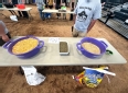 A table with tubs of grain on it and 2 people near it.