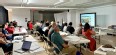 Conference room with people seated at long tables watching a PowerPoint presentation
