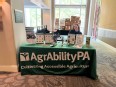 AgrAbility PA display table with a young woman sitting behind it smiling at the camera