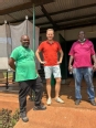 Mutumba Faisal standing next to a white man and another black Ugandan man on atin-roof covered porch